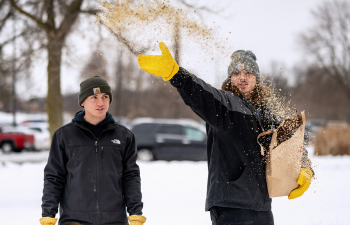 Two male students throw prairie seeds during the winter so they grow in the spring