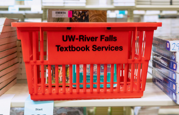 A red basket reading "UW-River Falls Textbook Services" sits on a shelf surrounded by textbooks