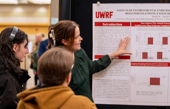 A woman presents her research poster to community members during the URSCA Fall Gala