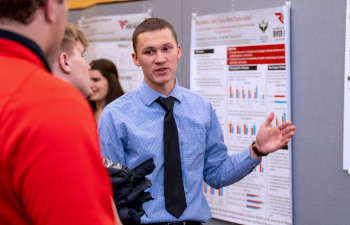 A male student presents his research poster to community members during the URSCA Fall Gala