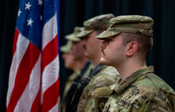 Military service member stand at attention holding flags during Commencement