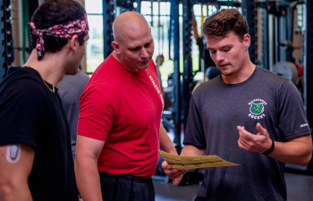 A personal trainer helps two students during their workout