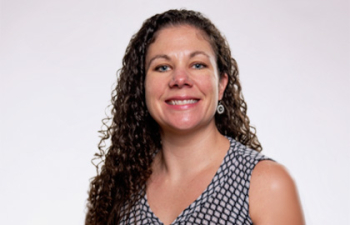 Headshot of Cristy Boyer, a woman with long curly brown hair wearing a black and white patterned tank top