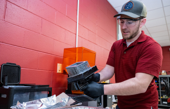 A male student inspects their 3D print in the 3D printing lab