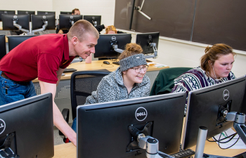 Professor  Patrick Woolcock looks over the shoulder of a female student at their computer screen