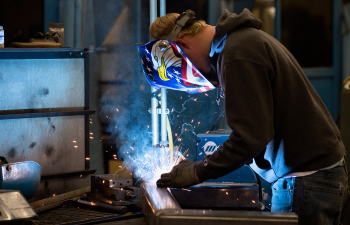 An engineering technology student welds two pieces of metal together in a shop