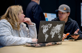 A male and female student talk with a laptop open facing them