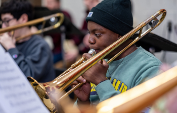 a male student wearing a blue shirt and black hat plays a trombone