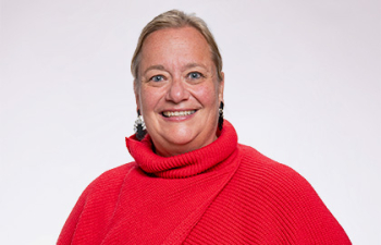 Headshot of Jenn Rassett, a middle aged woman with slicked back blonde hair wearing a bright red sweater.