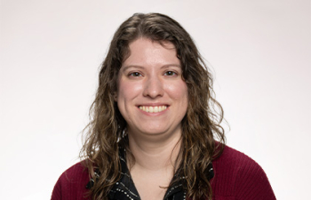 Headshot of Kaitlin Wilsey, a young woman with curly long brown hair wearing a red cardigan
