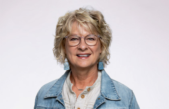 Headshot of Kristin Barstad, a middle aged woman with short blonde hair and glasses wearing a jean jacket
