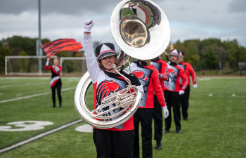 a marching band member holds a tuba and one arm in the air