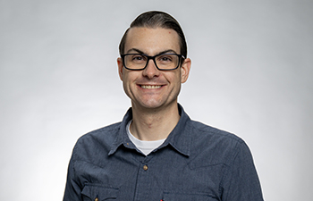 headshot of a white male with short dark hair. He's wearing a blue button up shirt and glasses.