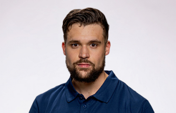 Headshot of Olaf Nelson, a young man with brown cropped hair and a long beard wearing a blue polo shirt