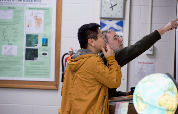 A professor points to a point on a map on the wall