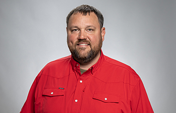 Ryan Bench headshot. A white male with short brown hair and brown facial hair is wearing a red button up shirt.