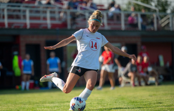 a women's soccer player wearing a white jersey and black shorts kicks the ball during a game