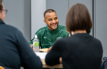 a man sits at a table and smiles at someone off screen