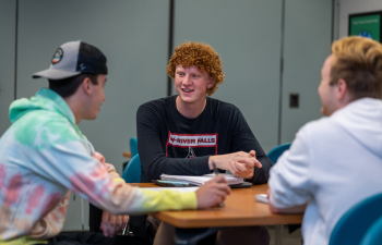 a student sits at a table and talks with two other students