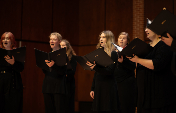 choir singers wearing all black hold song books and perform on a stage