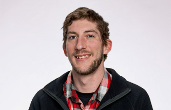 Headshot of Trent Rothstein, a young man with short brown hair wearing a black jacket with UW-River Falls stitched on