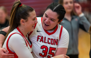 two women's basketball players wearing white Falcons uniforms embrace on the court after a game