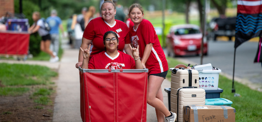 One girl sitting in a cart with two girls standing behind it