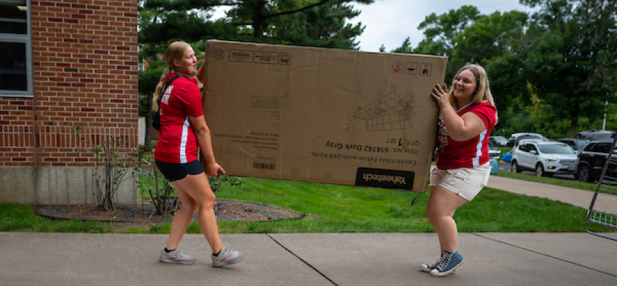 Two girls carrying a large TV into a building