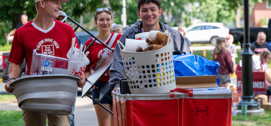 Three students helping move items in a cart