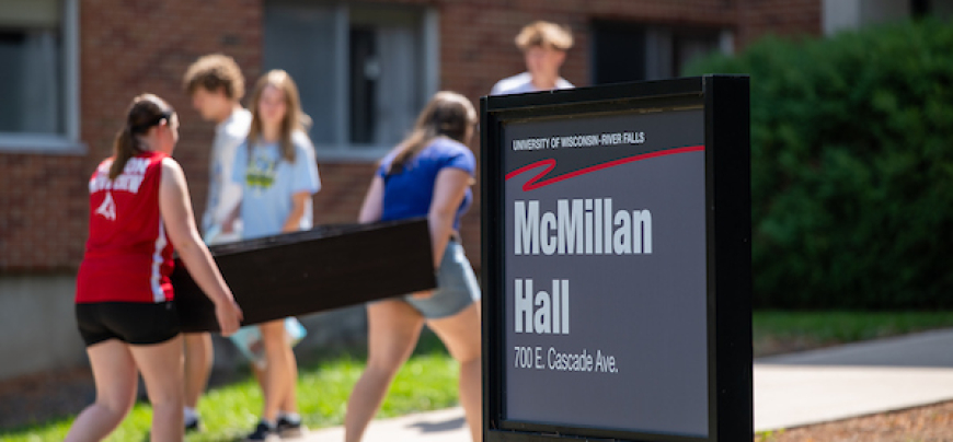 Two students carrying an object behind a building sign